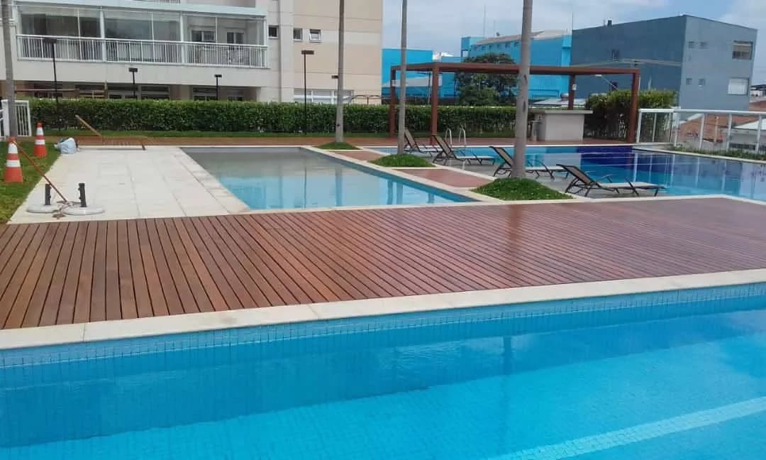 Deck de madeira instalado ao redor de piscinas em área de lazer de condomínio