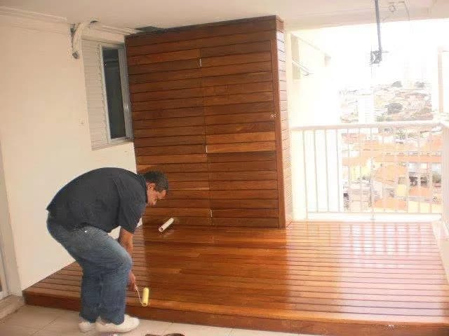 Profissional aplicando verniz em deck e painel de madeira em varanda de apartamento