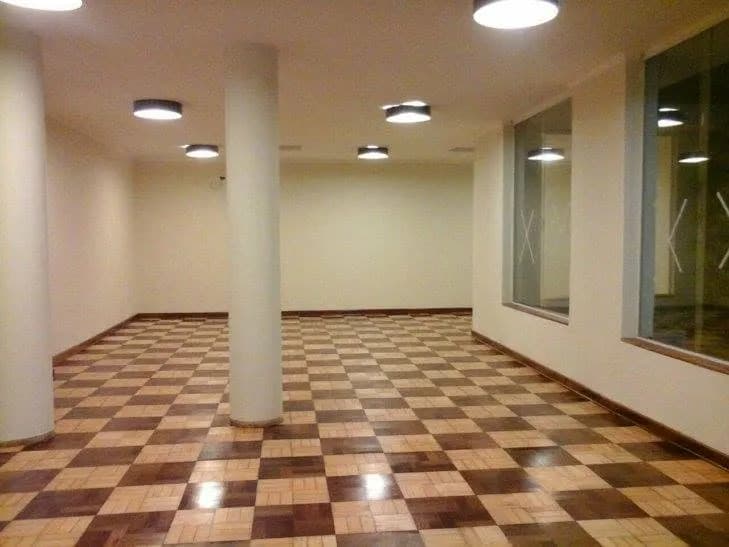 Salão comercial amplo com piso de tacos em padrão xadrez e colunas brancas